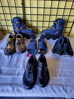 Overview photo showing five pairs of footwear: inline roller blades, two pairs of lace shoes, and two pairs of slip-on shoes arranged on a cloth with a grid background.