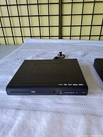 Front view of black Electcom Pro DVD player with DVD logo, power cable visible behind