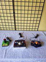 Three different vintage handheld TV games laid out on a white cloth, each with cable antenna and control buttons or joystick visible.