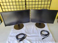 Two Lenovo ThinkPad monitors side by side, each with a circular base and cables coiled in front