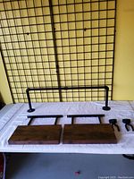 Black metal pipe bar with two round flange wall mounts, two wooden shelves with metal brackets, and two metal hook-style supports laid out on white sheet