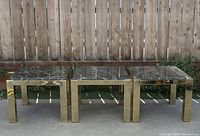 Three mid-century style side tables with gold brass bases and black marble tops, arranged in a row outdoors.