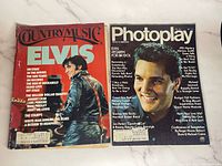 Two magazines laid side by side: on the left is a Country Music magazine with Elvis Presley on the cover; on the right is a Photoplay magazine featuring Elvis Presley on the cover.