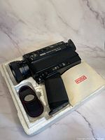Eumig Makro Sound 65 XL film camera displayed in white foam packaging with user manual and carrying pouch beside it.