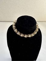 Front view of the goldtone bracelet with faux pearl links displayed on a black stand.