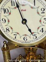 Close-up of clock face showing floral garland decoration, black Arabic numerals, black spade hands, and 'Made in Germany' marking.