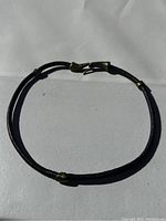 Full view of black leather choker with brass hardware laid flat on white background.