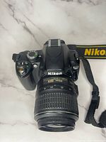 Front view of Nikon digital camera body with 18-55mm DX lens and Nikon neck strap.