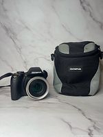 Olympus camera next to Olympus carrying case on white marble background.