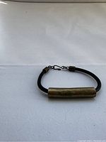 Photo showing the Osei-Duro hand cast brass tubular bracelet laid flat, with visible black leather cord and brass tube with clasp.