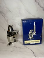 Front view of silver plated penguin candle holder with original blue box showing product illustration and text.
