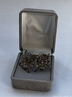Two sterling silver floral screw back earrings displayed in a gray velvet and satin-lined jewelry box.