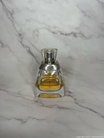 Front view of vintage Vera Wang perfume bottle showing amber liquid inside and clear thick glass with silver neck and square cap.