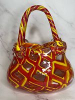 Front angled view of vintage red, yellow and clear glass purse-shaped vase or basket showing geometric pattern and twisted handle