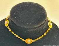 Gold-tone bracelet laid out on a black velvet jewelry display with three oval links, each containing a single white cultured pearl.