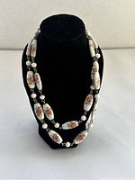 Front view of vintage porcelain rose bead necklace displayed on a black bust, showing detailed pink rose designs on porcelain beads and gold spacer beads.
