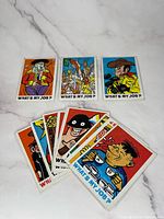Front side of several vintage "What’s My Job?" cards showing colorful cartoon characters like a cowboy, policeman, masked burglar, and others.