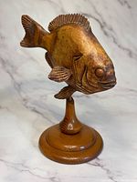 Front and side views of a handmade wooden sunfish sculpture on a rounded wooden base, showing carved details and natural wood grain finish.