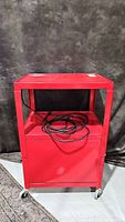 Red Bretford Model E AV cart with castor wheels seen from front with electrical cord inside the shelf.