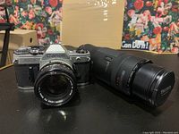 Canon AE-1 film camera with 50mm f/1.4 lens mounted and 100-300mm f/5.6 zoom lens beside it on a table.