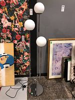 Full view of the IKEA Simrishan floor lamp showing three white globe lampshades on chrome stand with power cord visible on the floor.