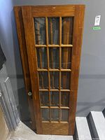 Front view of one wood framed French door with multiple glass panes, showing wood grain and doorknob.