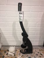 Full view of the C.S. Osborne hand press machine showing the lever handle and press base with a white spherical accessory next to it.