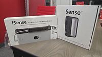 Boxes of iSense 3D scanner for iPad mini with Retina display and Sense 3D scanner on a wood table against red office background.