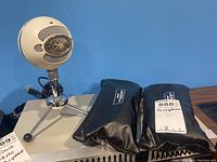 Blue Snowball USB microphone on tripod stand with two black zippered pouches containing Transcontinental microphones on table against blue wall.