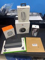 Photo showing all items boxed and packaged: Google Nest Thermostat, iPhone 4, Godox R1 RGB light, Logitech mouse, Belkin mini iPad case, and brown box with wall plate cover.