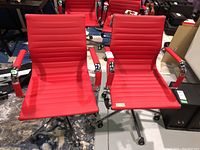 Front view of two red faux leather Structube task chairs with visible horizontal channel stitching and chrome armrests and bases.