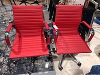 Pair of red faux leather Structube task chairs shown side by side on a carpeted floor, with visible tags and chrome metal armrests and wheeled bases.