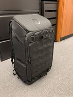 Front angled view of the black Tenba camera backpack showing its vertical rectangular shape and webbing details on the front and sides.