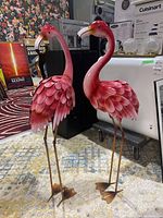Two decorative tin flamingos side by side showing front view