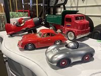 All four model toy vehicles displayed on a white table: Porsche 356 B, Tonka dump truck, red/black biplane, silver race car