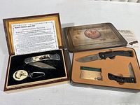 Two sets of hunting knives, Buck Boone and Crockett set with two folding knives in foam-fitted metal case; Maxam set with folding knife and eagle keychain in woodgrain decorative case.