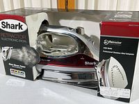 Photo showing Shark Retractor Electronic Iron in original box with branding, model number G1477RN, and product features.