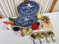 Display of two ceramic vegetable plaques with accessory hooks, ceramic vegetable garland, and two blue and white metal farmhouse-style serving bowls on a table.