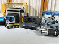 Photo showing Polaroid Impulse, Kodak Handle camera in box, and Vivitar binoculars/camera combo.