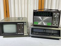 Goldstar 5 inch portable B/W TV with AM/FM stereo radio on the left, Kresge Company portable AM/FM radio on top right, and General Electric tabletop clock radio below the radio.