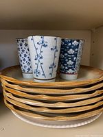 Stack of speckled tan Whole Wheat Granola dinner and side plates with three blue floral patterned green tea cups on top.
