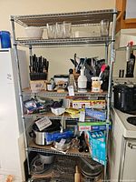 Full view of the metal wire shelving rack loaded with kitchen items (not included in lot). Chrome wire shelves and tubular frame.