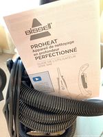Photo showing Bissell ProHeat user manual with hose wrapped around the cleaner handle