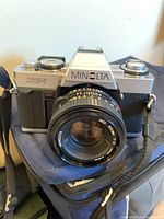 Front view of Minolta XG-1 camera with attached Minolta MD 50mm f/2 lens on blue carrying bag.