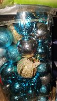 Box of assorted blue, silver, and gold Christmas ball ornaments in clear plastic container