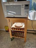 Wooden kitchen stand with microwave and cutting boards from side view showing overall setup and floor surface.