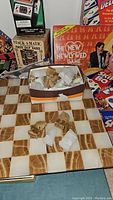 Marble chess board with carved brown and white marble chess pieces in front and vintage board games behind