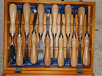 Top-down image showing all 12 chisels with wooden handles neatly arranged inside a fitted wooden box.