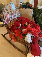 Mini wooden rocking chair with attached 'Ho Ho Ho' sign and poinsettia flowers, plus a Santa-style hat.