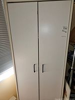 Closed white melamine cupboard with two black handles on doors.